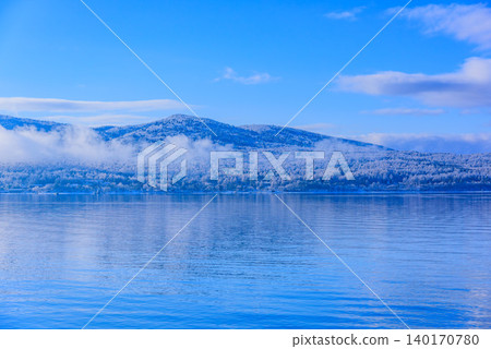 A minimalist background image of a winter lakeside enveloped in silence, with a clear blue sky and snow-covered trees. A minimalist background image of a winter lakeside enveloped in silence, with a clear blue sky and snow-covered trees. 140170780