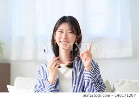 A Japanese woman pointing while holding her smartphone. A Japanese woman pointing while holding her smartphone. 140171207