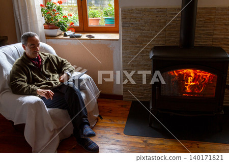 Senior Man Reading a Book on Sofa by Cozy Fireplace Senior Man Reading a Book on Sofa by Cozy Fireplace 140171821