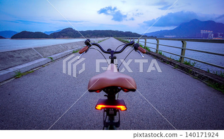 Riding a bicycle on a scenic coastal path at dusk with mountains in the background 140171924