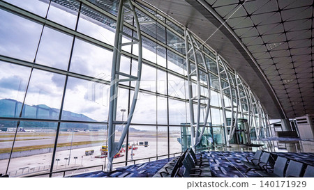 Modern Hong Kong airport terminal interior with large glass windows overlooking the tarmac and mountains Modern Hong Kong airport terminal interior with large glass windows overlooking the tarmac and mountains 140171929