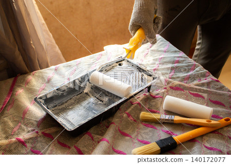 Hand dipping roller into paint tray. Self made home improvement on budget. Cosmetic renovation Hand dipping roller into paint tray. Self made home improvement on budget. Cosmetic renovation 140172077