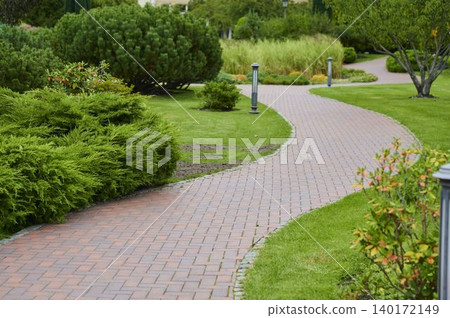 Winding brick path through a vibrant green garden filled with lush plants Winding brick path through a vibrant green garden filled with lush plants 140172149