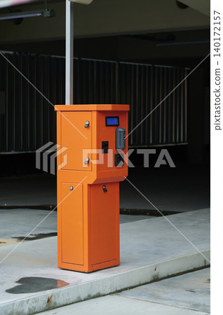 Bright orange parking meter stands alone in a quiet garage in the late afternoon sunlight Bright orange parking meter stands alone in a quiet garage in the late afternoon sunlight 140172157