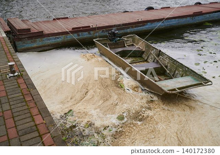 Faded boat rests quietly on the shore as water pollution dances around its hull Faded boat rests quietly on the shore as water pollution dances around its hull 140172380