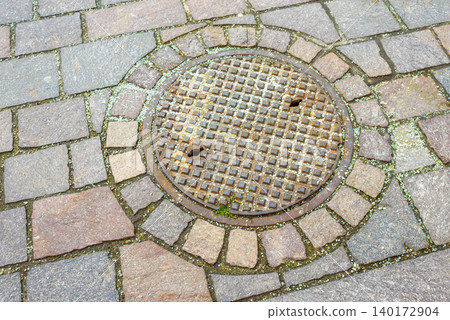 Rusty manhole cover surrounded by old cobblestones Rusty manhole cover surrounded by old cobblestones 140172904