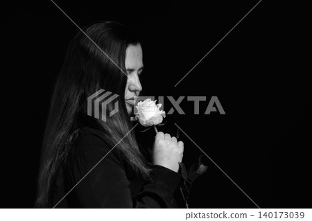 profile portrait of a woman in dark clothing closely inhaling the fragrance of a rose 140173039