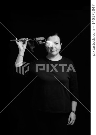 portrait of a woman with a white rose by her eye on a black background 140173047