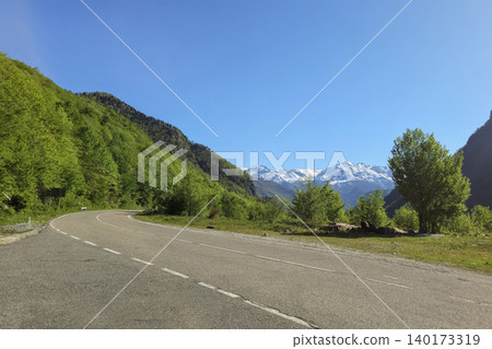 Winding road hugs lush green hills under clear blue sky Winding road hugs lush green hills under clear blue sky 140173319