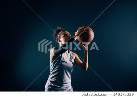 A female basketball player prepares to throw a ball against black background A female basketball player prepares to throw a ball against black background 140173329