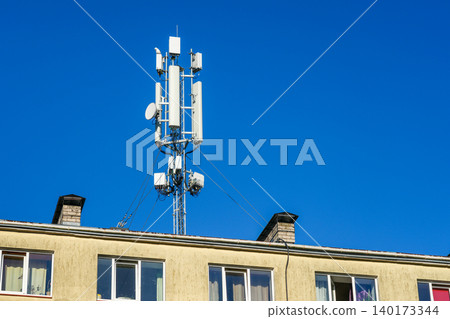 Cellular communication tower mounted on residential building rooftop against clear blue sky backdrop Cellular communication tower mounted on residential building rooftop against clear blue sky backdrop 140173344