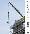 Tower crane lifting concrete block during multi story building construction with scaffolding work 140173348