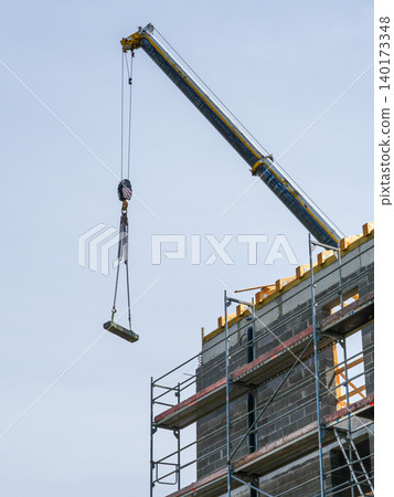 Tower crane lifting concrete block during multi story building construction with scaffolding work Tower crane lifting concrete block during multi story building construction with scaffolding work 140173348