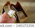 Hand holding euro banknotes near grocery shopping bags with food purchases and rising living costs 140173356