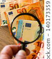 Magnifying glass inspecting euro banknotes for authenticity, finance security and fraud detection 140173359