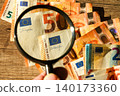 Magnifying glass examining euro banknotes for authenticity, fraud detection and financial security 140173360