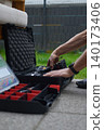 Hands place cordless drill into tool case on paving beside grass 140173406
