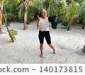Young happy woman volunteer holding a black bag and showing a thumbs up while standing in a tropical environment 140173815
