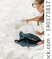 High angle of young woman picking up plastic bottle from white sand 140173817
