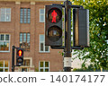 Red Pedestrian Signal Stands Tall Amidst the Vibrant City Center of Amsterdam, Guiding Footsteps Safely Across the Bustling Streets 140174177