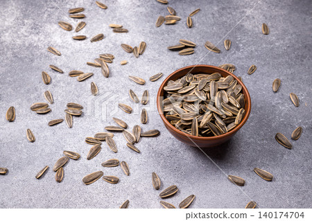 Sunflower seeds spilling from a bowl on a gray background Sunflower seeds spilling from a bowl on a gray background 140174704