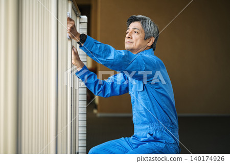 A senior male building manager cleans the railings of an apartment building with a rag. A senior male building manager cleans the railings of an apartment building with a rag. 140174926