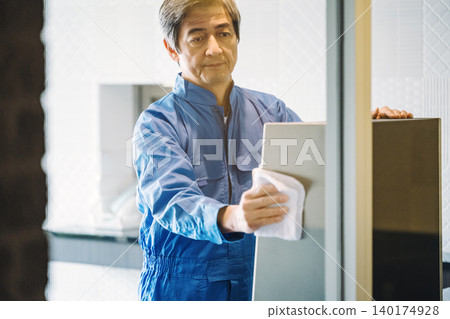 A senior male building manager cleaning the inside of the apartment building with a rag. A senior male building manager cleaning the inside of the apartment building with a rag. 140174928
