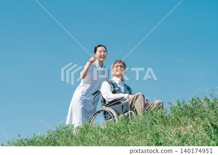 A nurse in a white coat and a senior man walking in a wheelchair A nurse in a white coat and a senior man walking in a wheelchair 140174951