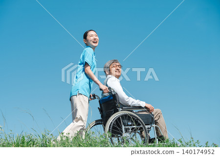 一位護理人員和一位坐在輪椅上的老人沿著河岸散步。 一位護理人員和一位坐在輪椅上的老人沿著河岸散步。 140174952