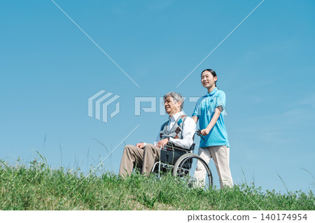 一位護理人員和一位坐在輪椅上的老人沿著河岸散步。 140174954