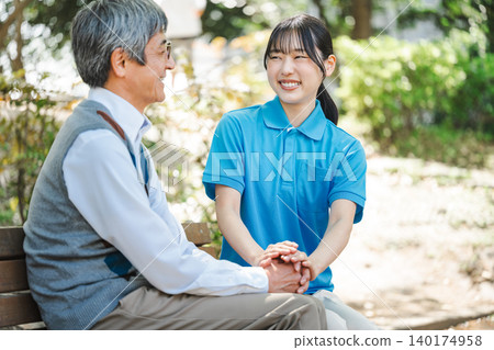 一位年輕的護理員坐在公園長椅上,旁邊有一位老人。 一位年輕的護理員坐在公園長椅上,旁邊有一位老人。 140174958