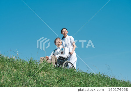 A nurse in a white coat and a senior man walking in a wheelchair A nurse in a white coat and a senior man walking in a wheelchair 140174968