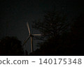 Wind turbines and tree silhouettes turning under a sky full of stars. 140175348