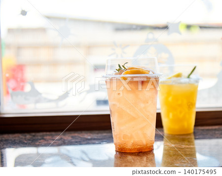 Fresh iced citrus beverages in transparent takeaway cups displayed on cafe table by bright window, showcasing refreshing summer drinks, healthy lifestyle refreshment, modern coffee shop ambiance and 140175495