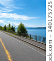 A scenic drive along a road overlooking a blue sky and lakeside. 140175725