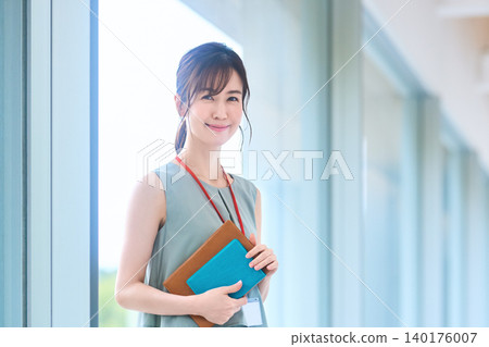 An office woman smiles, wearing her employee ID badge and holding her notebook. An office woman smiles, wearing her employee ID badge and holding her notebook. 140176007