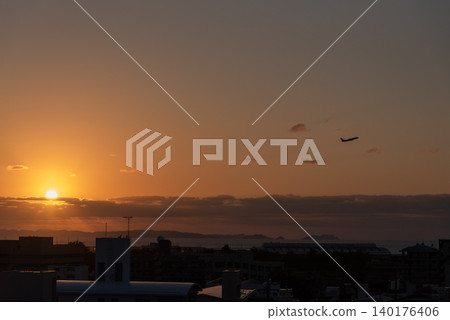 An orange sunset sky with a plane taking off, a city silhouette in the foreground, the sun, and a remote island visible in the distance. An orange sunset sky with a plane taking off, a city silhouette in the foreground, the sun, and a remote island visible in the distance. 140176406