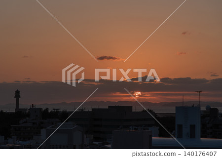 The orange sunset sky has the silhouette of a city in the foreground, and the sea with a remote island visible in the distance. The orange sunset sky has the silhouette of a city in the foreground, and the sea with a remote island visible in the distance. 140176407
