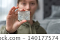 Teenager holding a pack of one-day contact lenses in a bedroom setting, soft lighting and blurred background elements visible 140177574
