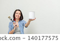 Woman holding paint can and brush in home renovation mockup, showcasing a blank wall ready for painting in a modern interior setting 140177575