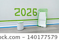 Home construction scene with paint can, roller tray, and green painter's tape marking the year 2026 on a wall in a modern interior 140177579