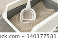 Cat litter box with scoop placed inside, featuring clean sand and a modern design on a textured floor in a home setting 140177581