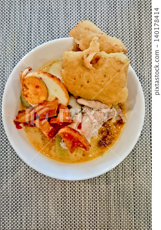 close-up photo of a bowl of lontong with potato sambal, egg, chicken and fried tempeh toppings on a white table close-up photo of a bowl of lontong with potato sambal, egg, chicken and fried tempeh toppings on a white table 140178414