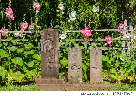 Hollyhocks and stone statues Hollyhocks and stone statues 140178804