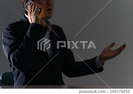 一名三十多歲的男子,面目模糊,在昏暗的房間裡使用智慧型手機進行詐騙活動。 一名三十多歲的男子,面目模糊,在昏暗的房間裡使用智慧型手機進行詐騙活動。 140178850