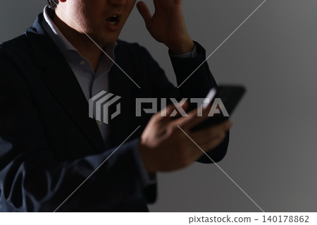 A man in his 30s, dressed in a suit and with his face obscured, was found in a dark room, clutching his head in front of his smartphone, having been the victim of a crime. 140178862