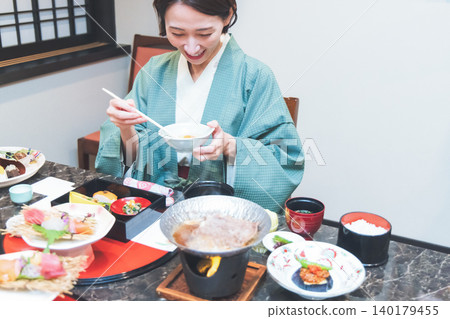 A woman in a yukata eating a kaiseki meal at a hot spring inn. A woman in a yukata eating a kaiseki meal at a hot spring inn. 140179455