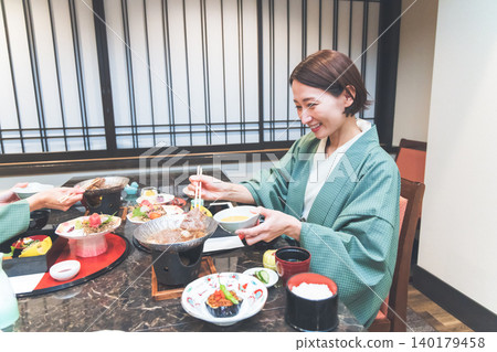 A woman in a yukata eating a kaiseki meal at a hot spring inn. 140179458