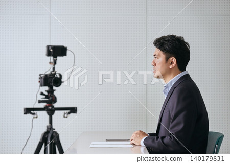 The image is of a Japanese male news anchor in his 30s, reporting and making announcements in front of a camera in a recording studio. The image is of a Japanese male news anchor in his 30s, reporting and making announcements in front of a camera in a recording studio. 140179831