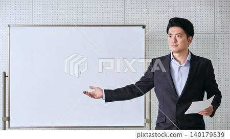 一位三十多歲的日本商人,手持文件,在辦公室會議室的白板前講解著什麼。 一位三十多歲的日本商人,手持文件,在辦公室會議室的白板前講解著什麼。 140179839